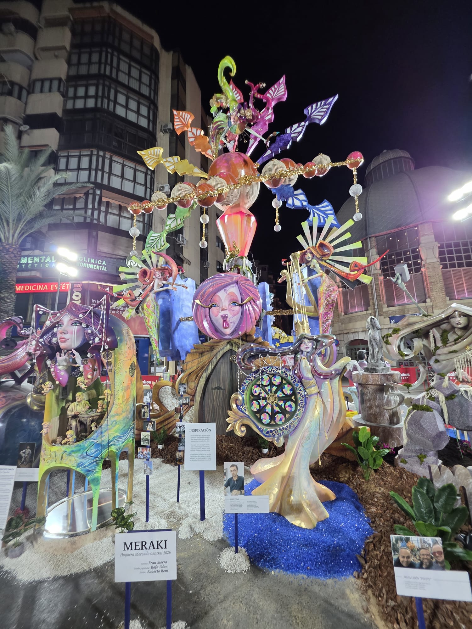 Vista frontal de la hoguera grande Mercado Central 2026 con cristal triturado azul, piedra blanca Macael, corteza de pino, rocallas y plantas decorativas instaladas por BMDP.